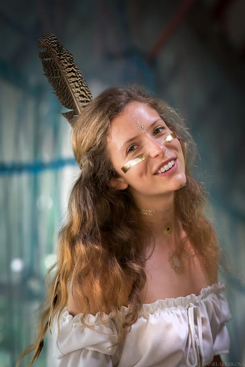 Smiling woman wearing a feather and gold face paint at a festival