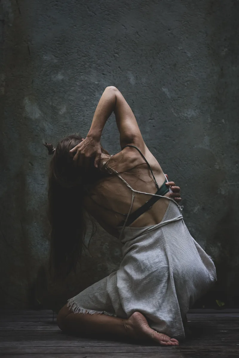 Woman in a flowing dress leaning back against a dark wall