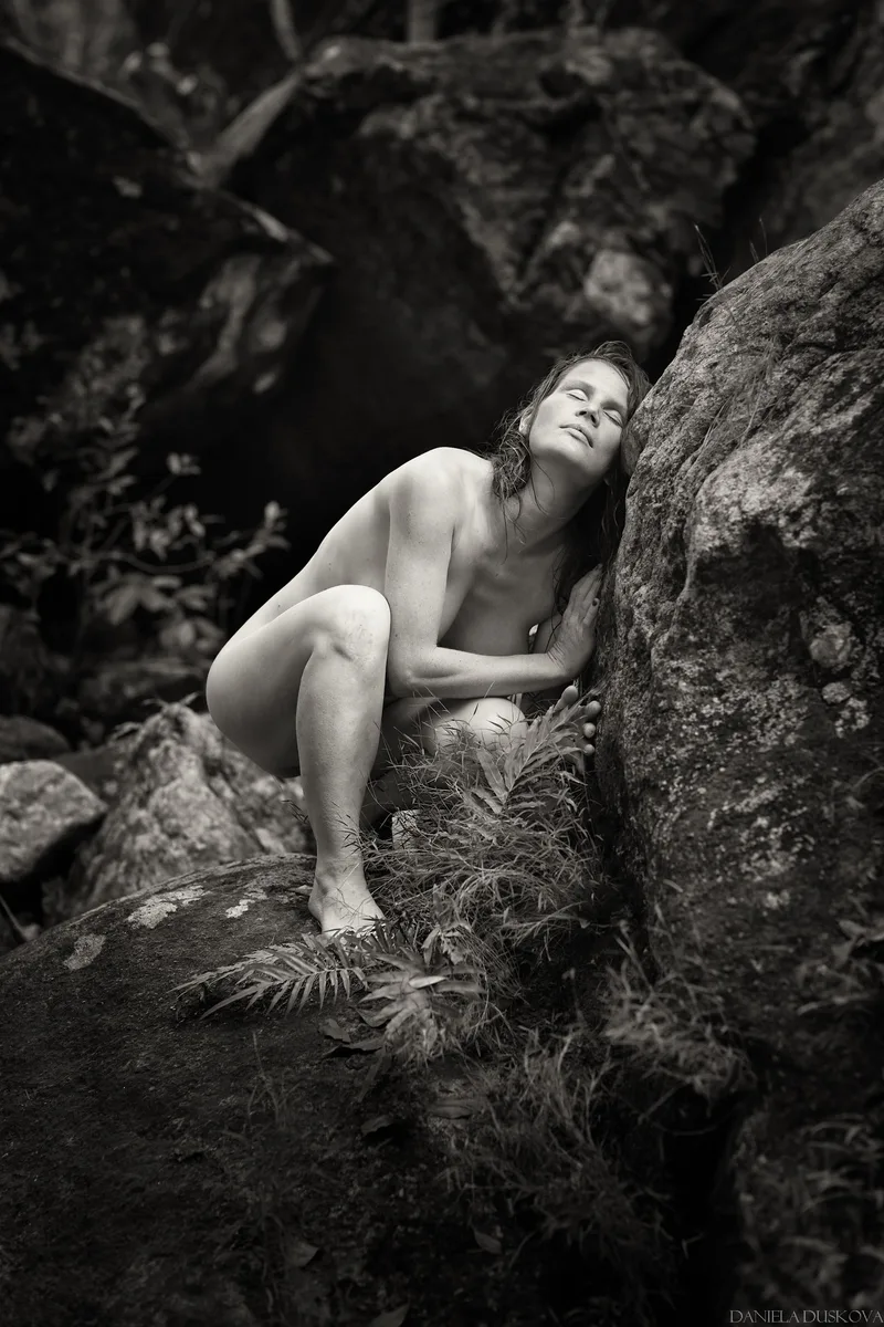 A woman leaning against a boulder in a forest portrait