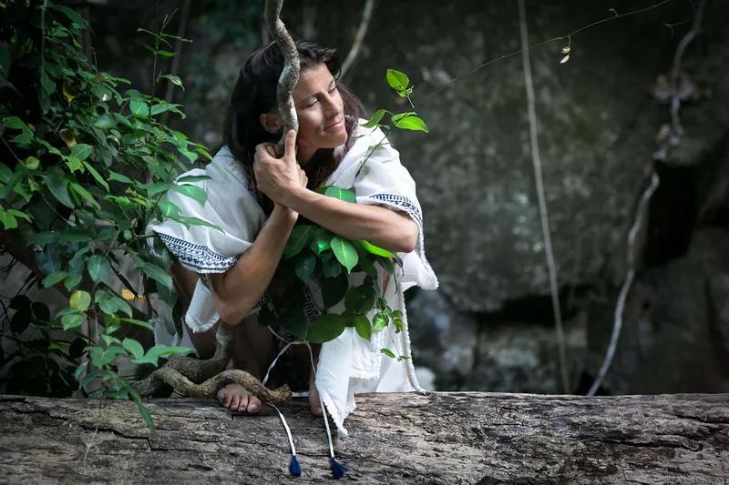 Woman in a white robe beside jungle rocks